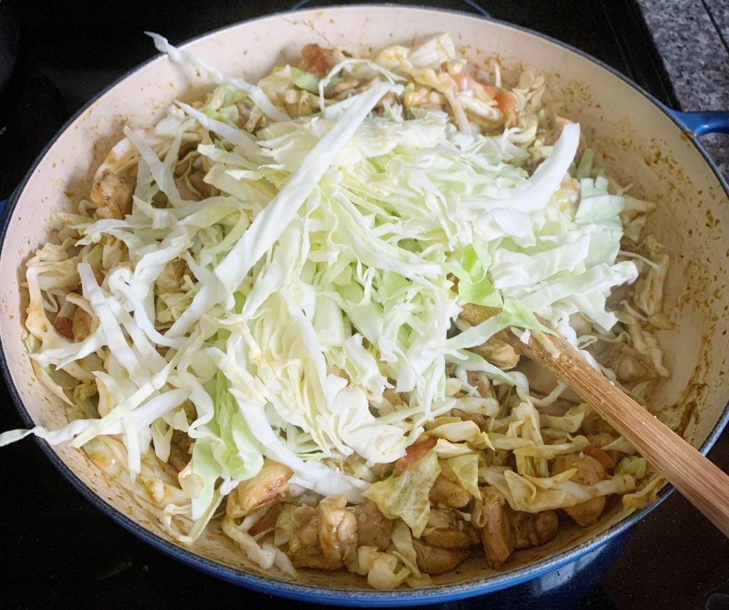 shredded cabbage added to skillet full of chicken