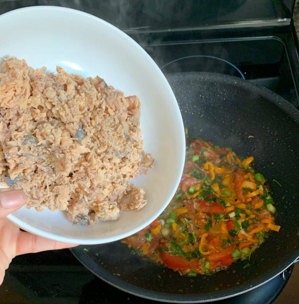 adding canned salmon to a wok pan with sauteed vegetables 