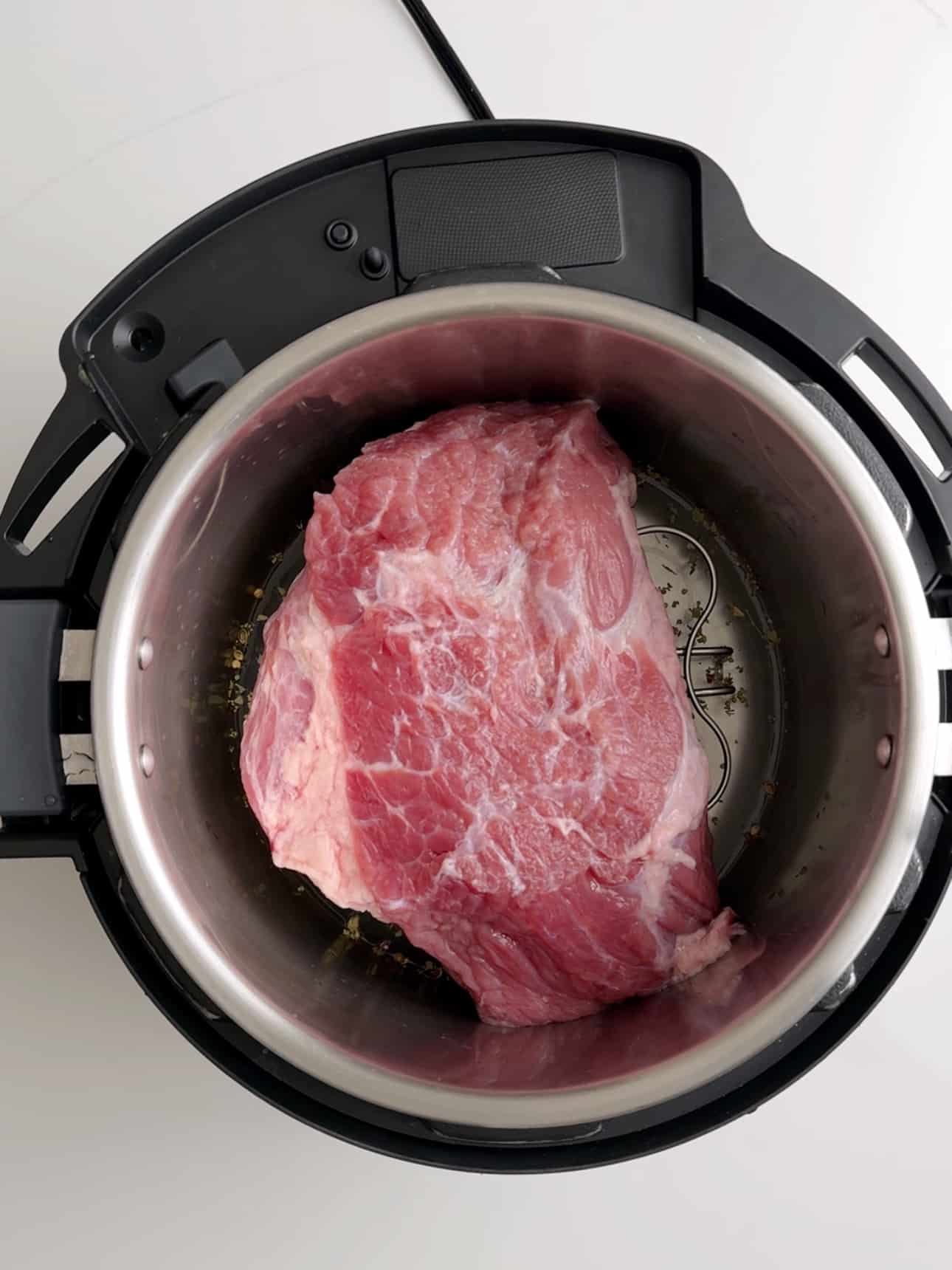 An instant pot with water and spices and a beef brisket on top of a trivet