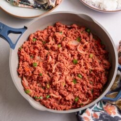 Jamaican Corned Beef in a gray skillet with a dish of rice to the right and a colorful napkin to the lower right.