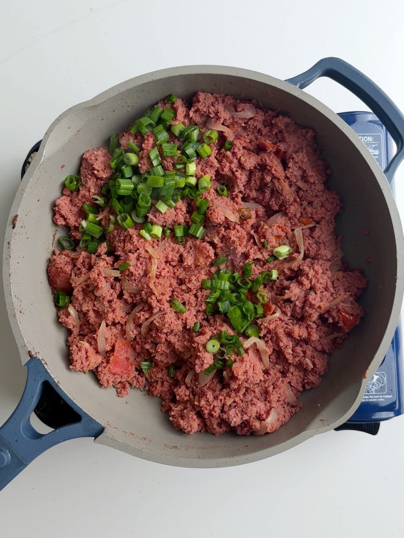 Adding scallions as a garnish for sautéed corned beef in a gray skillet