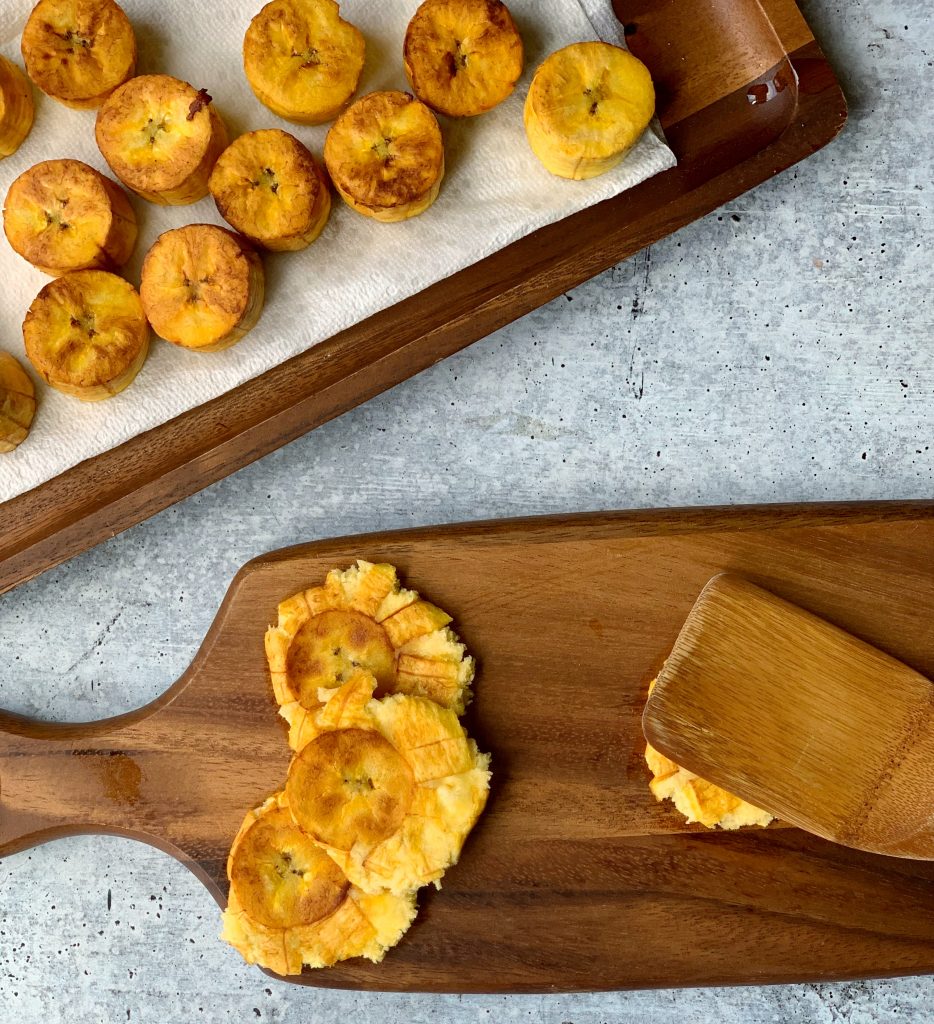 overhead view of a wooden spatula smashing plantains for tostones