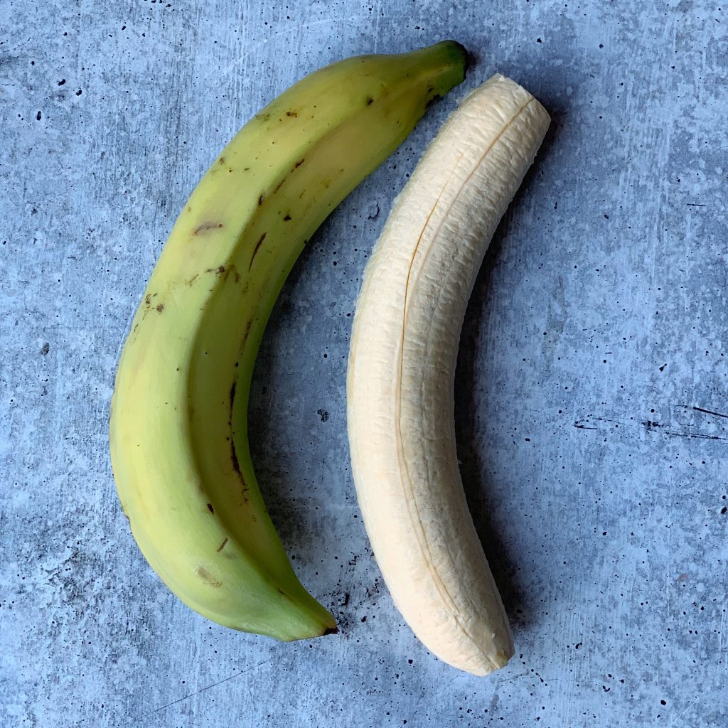 two green plantains, one with the peel on and one with the peel off