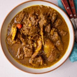 Guyanese lamb curry plated with two spoons with wooden handles, resting on a blue napkin to the upper right of the image