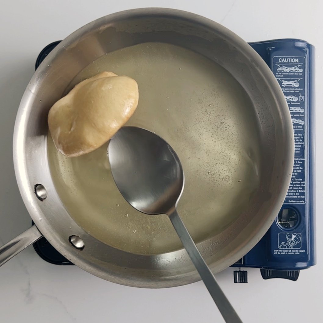 cooking bake in a frying pan. A metal spoon is tilting the bake forward.