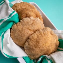 Gluten-free bakes in a while rectangular bowl resting on a teal back ground. The bakes are wrapped on a white towel with matching teal stripes.