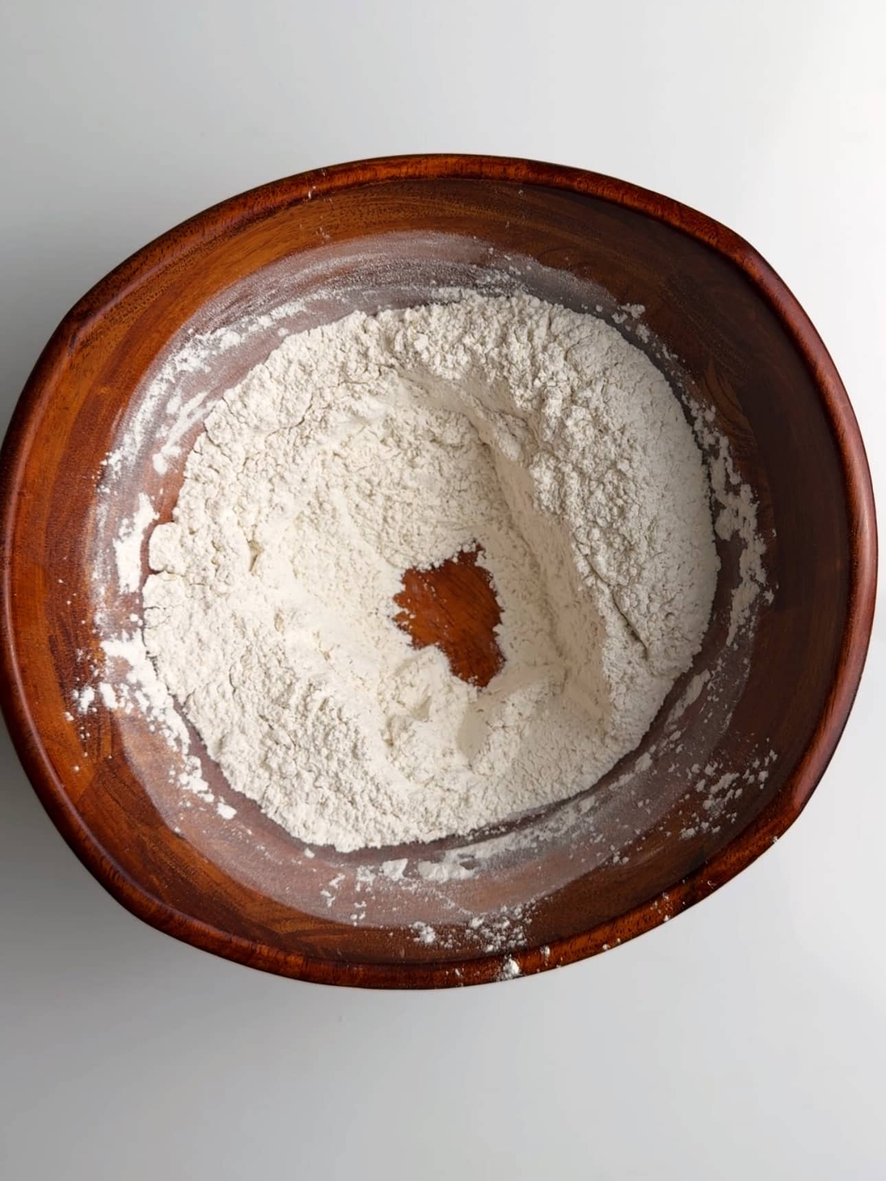 Dry ingredients in a wooden bowl with a well in the center showing the bottom of the bowl.