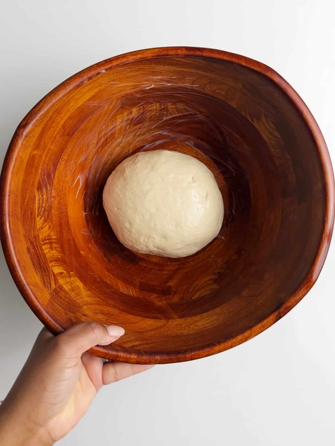 A small dough ball resting in a wooden bowl