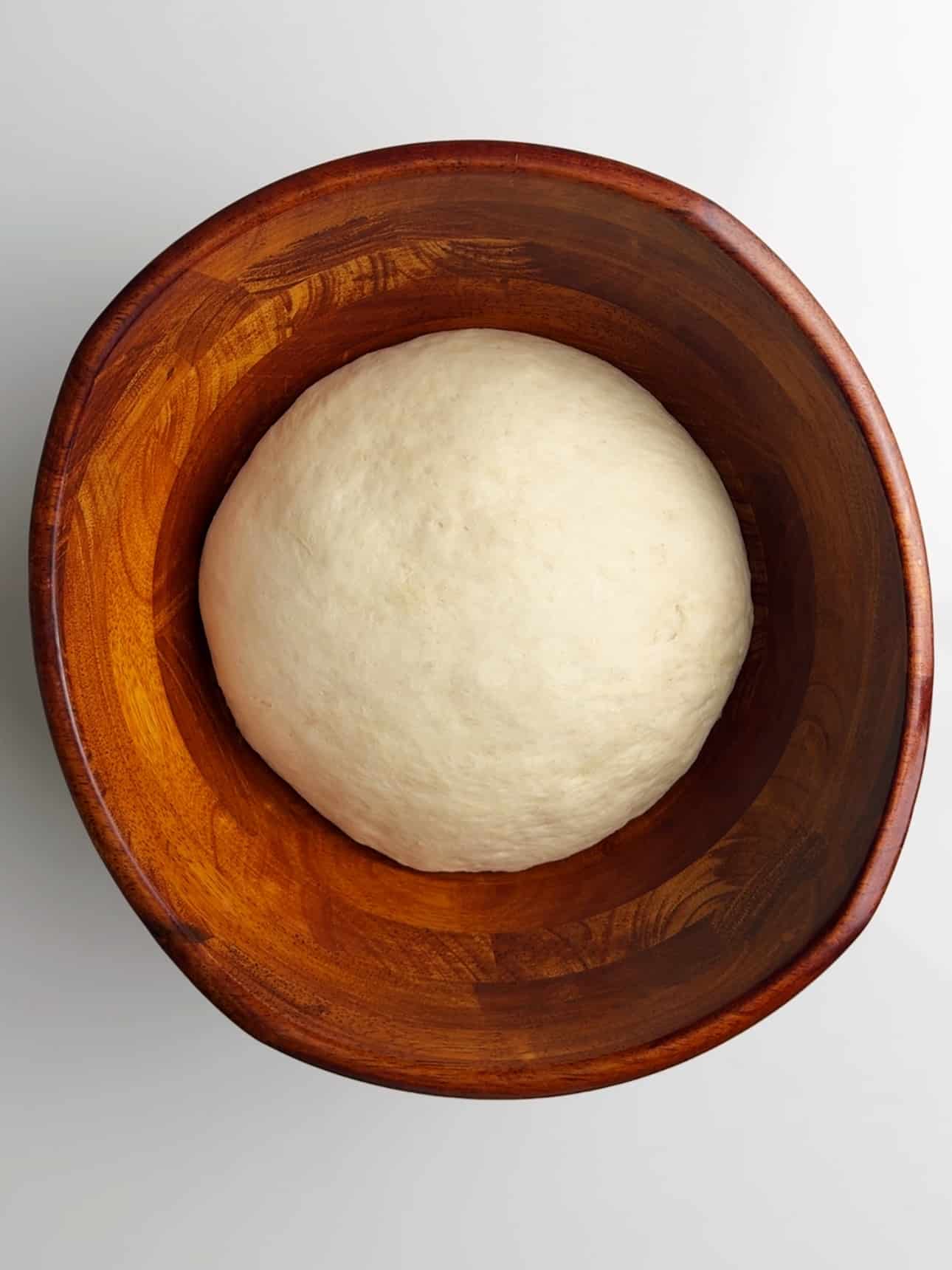 A large dough ball resting in a wooden bowl