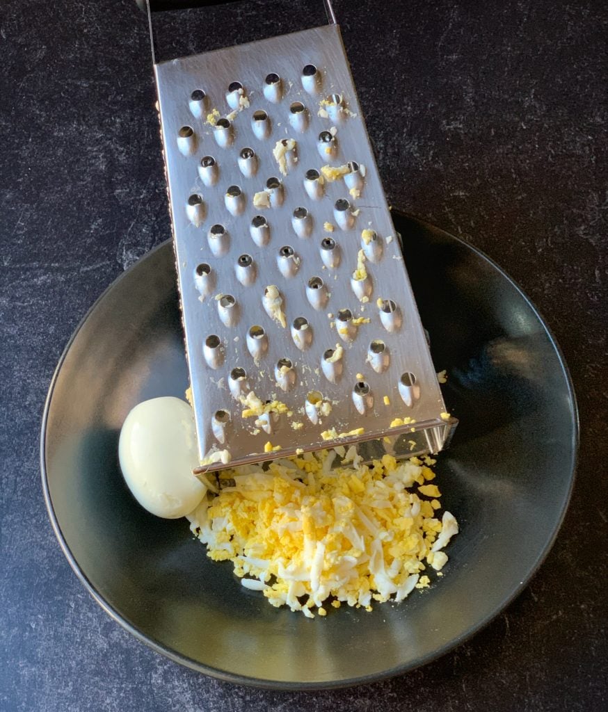 a grate being used to shred hard boiled eggs for egg salad