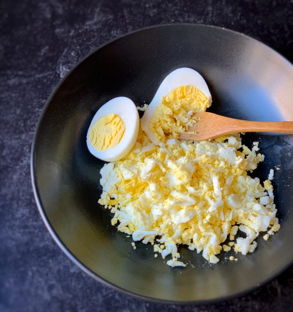 a wooden fork inserted into a bowl of hard boiled eggs to mash them