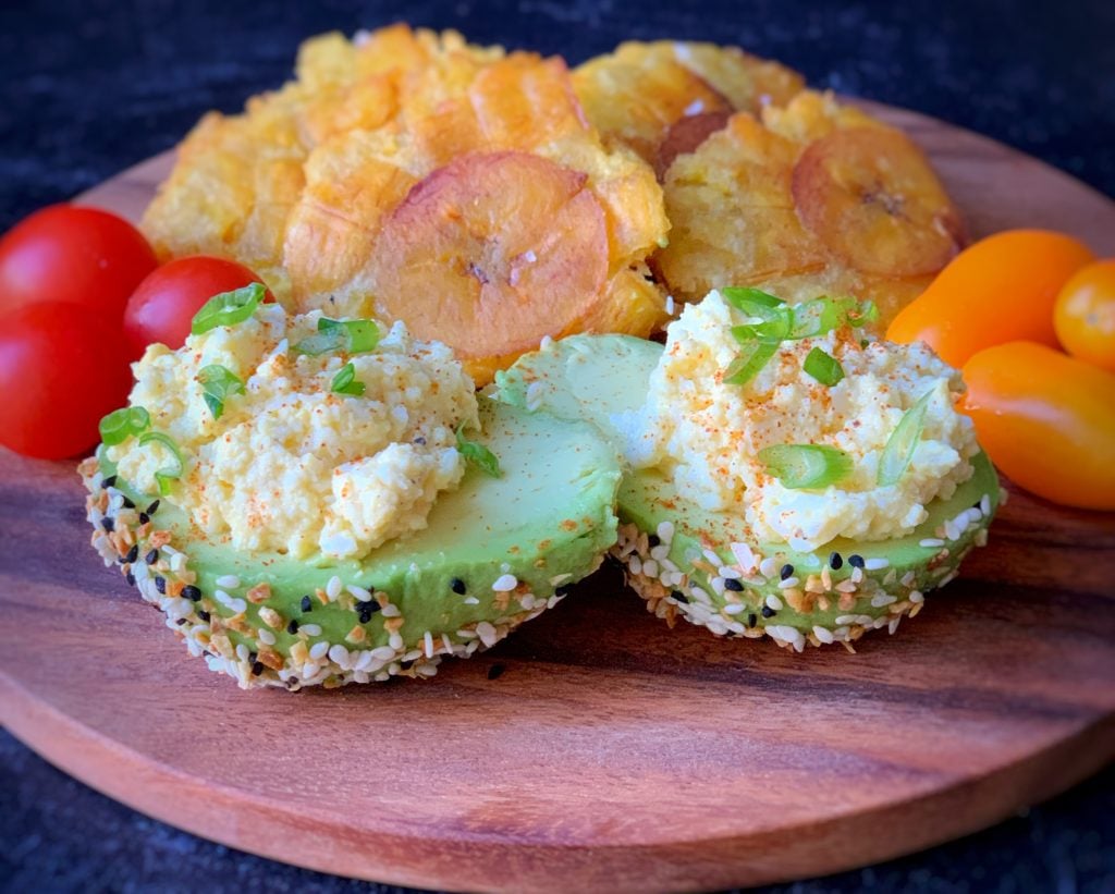 egg salad stuffed avocado on a platter with tomatoes and tostones