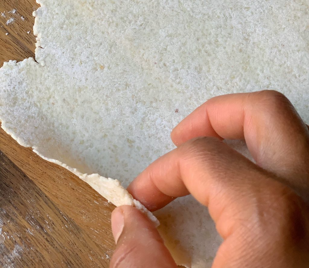 a finger pinching a rolled out grain free roti dough to show how thin it is