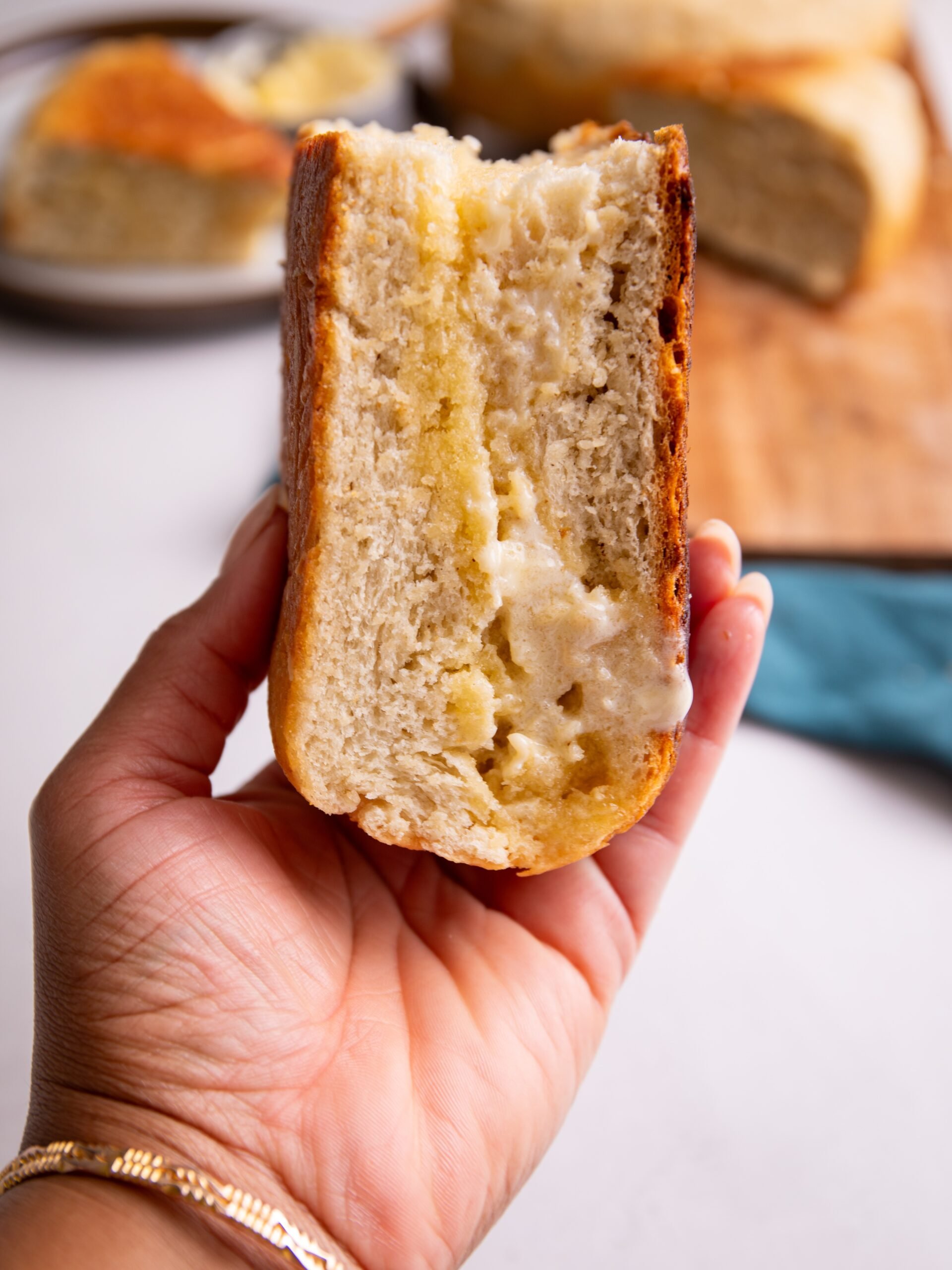 A slice of pot bake held in a brown hand. Butter is dripping from the cross section of the bake.