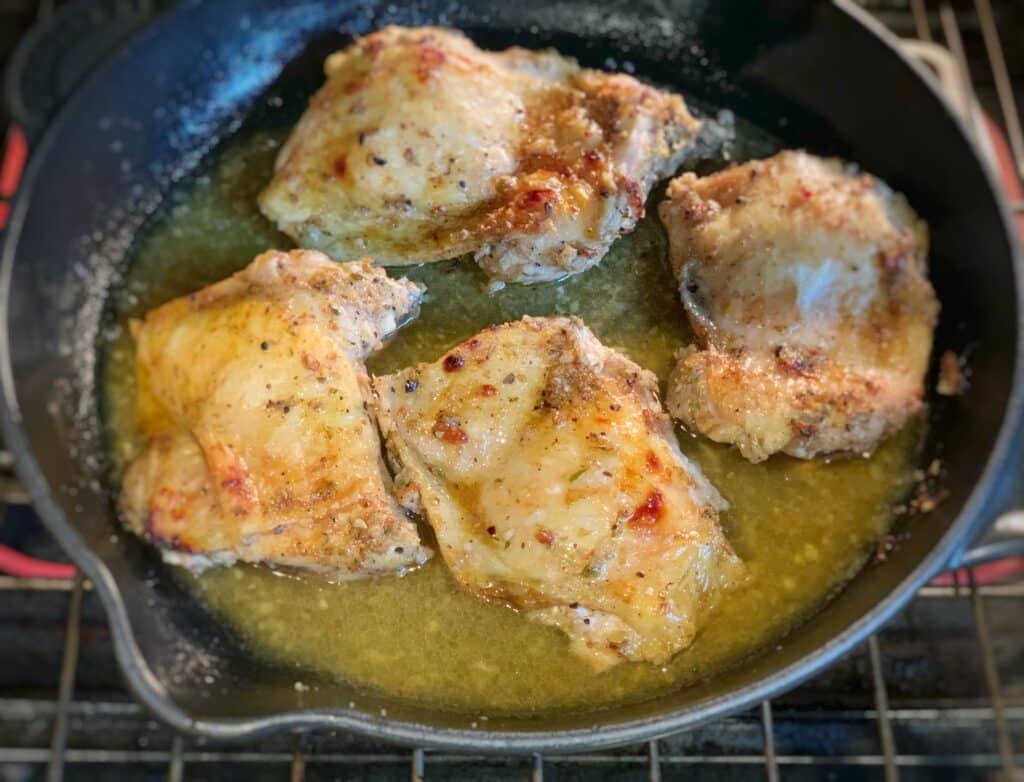 four chicken thighs roasting in a skillet