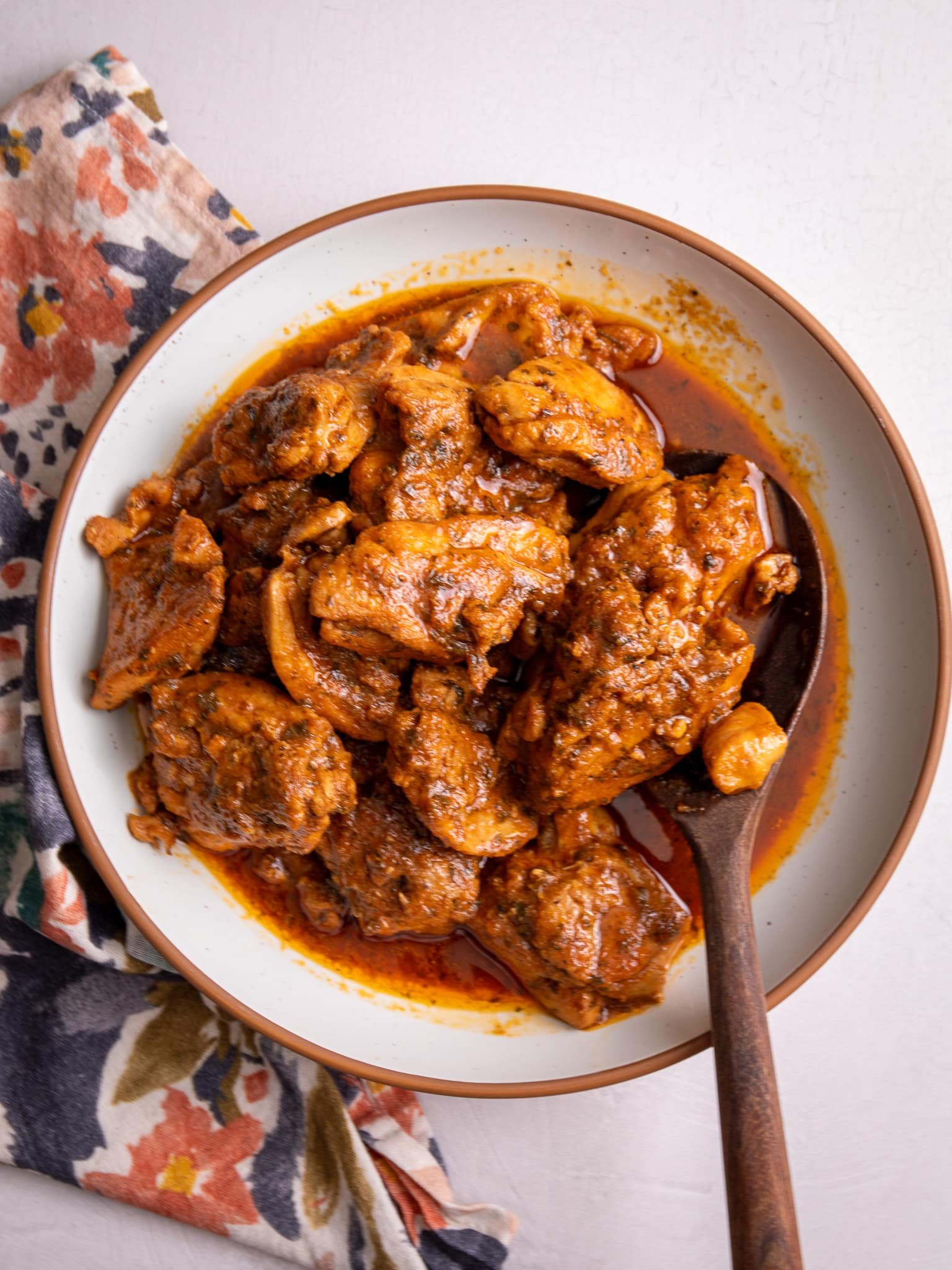 Caribbean Stew Chicken plated in a white bowl with a brown rim. A wooden spoon is scooping up some of the chicken.