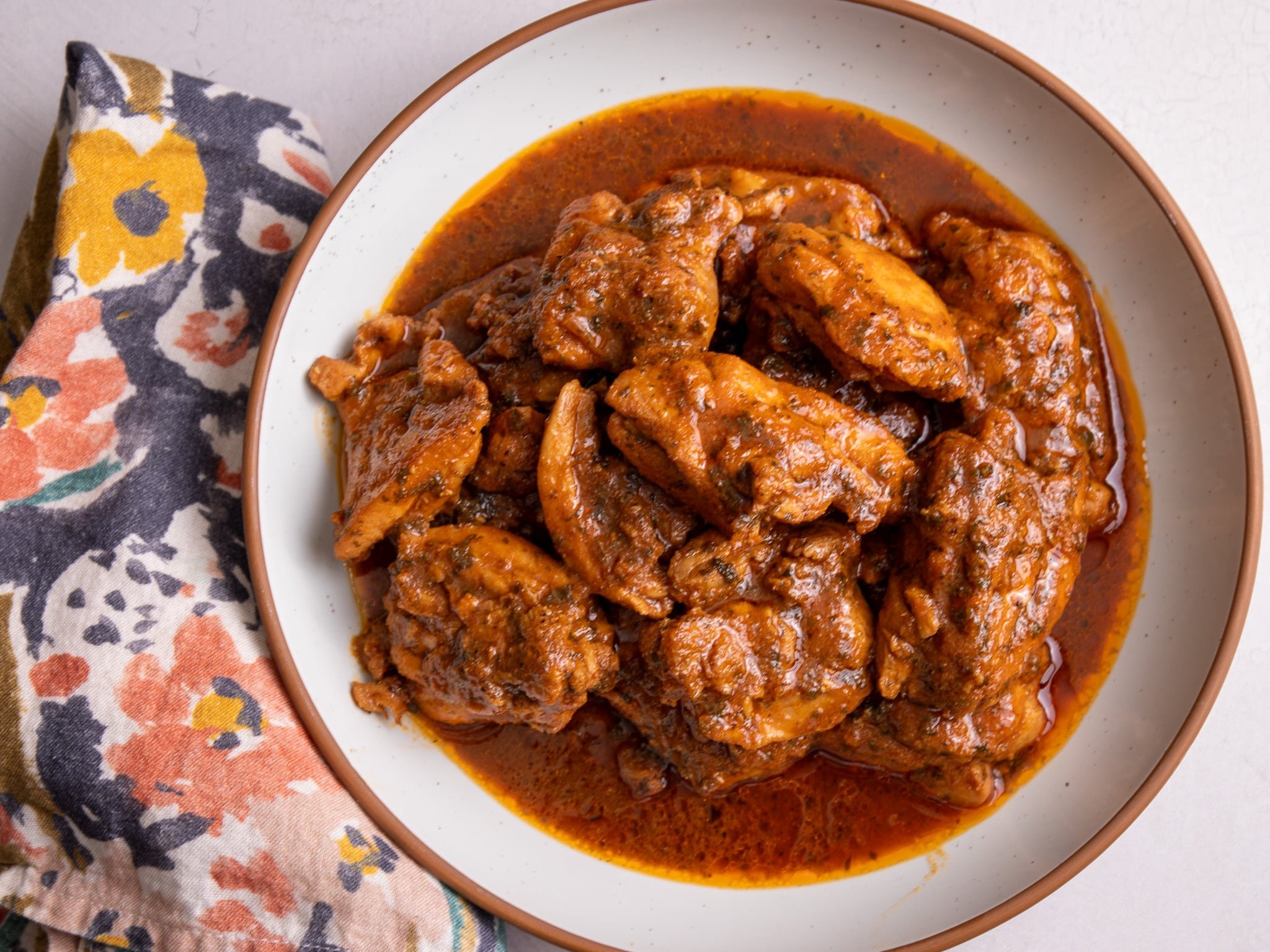 Caribbean Stew Chicken plated in a white bowl with a brown rim. A wooden spoon is scooping up some of the chicken.