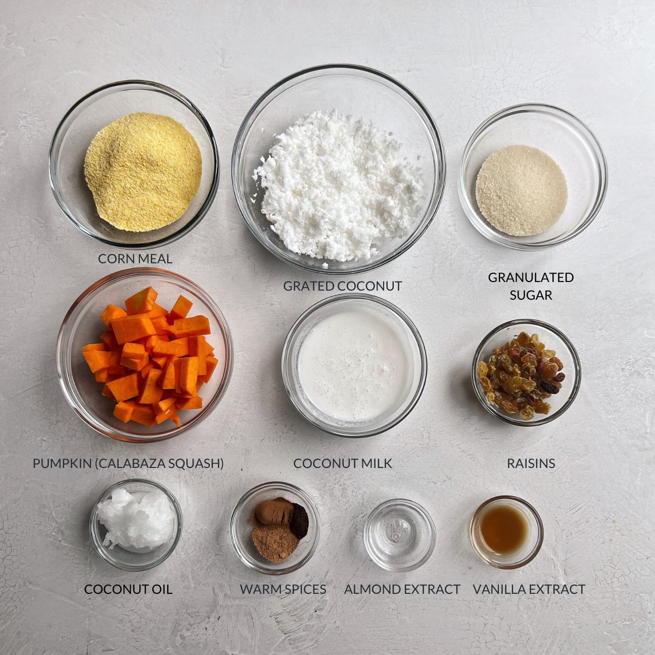 Ingredients for Guyanese Conkie measured out in glass bowls on a white concrete background