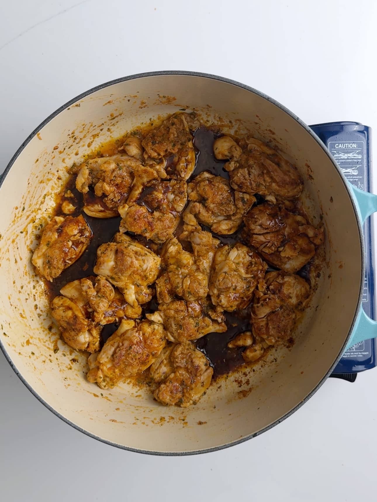 Coconut aminos has been added to the seared chicken thighs in a cast iron skillet.