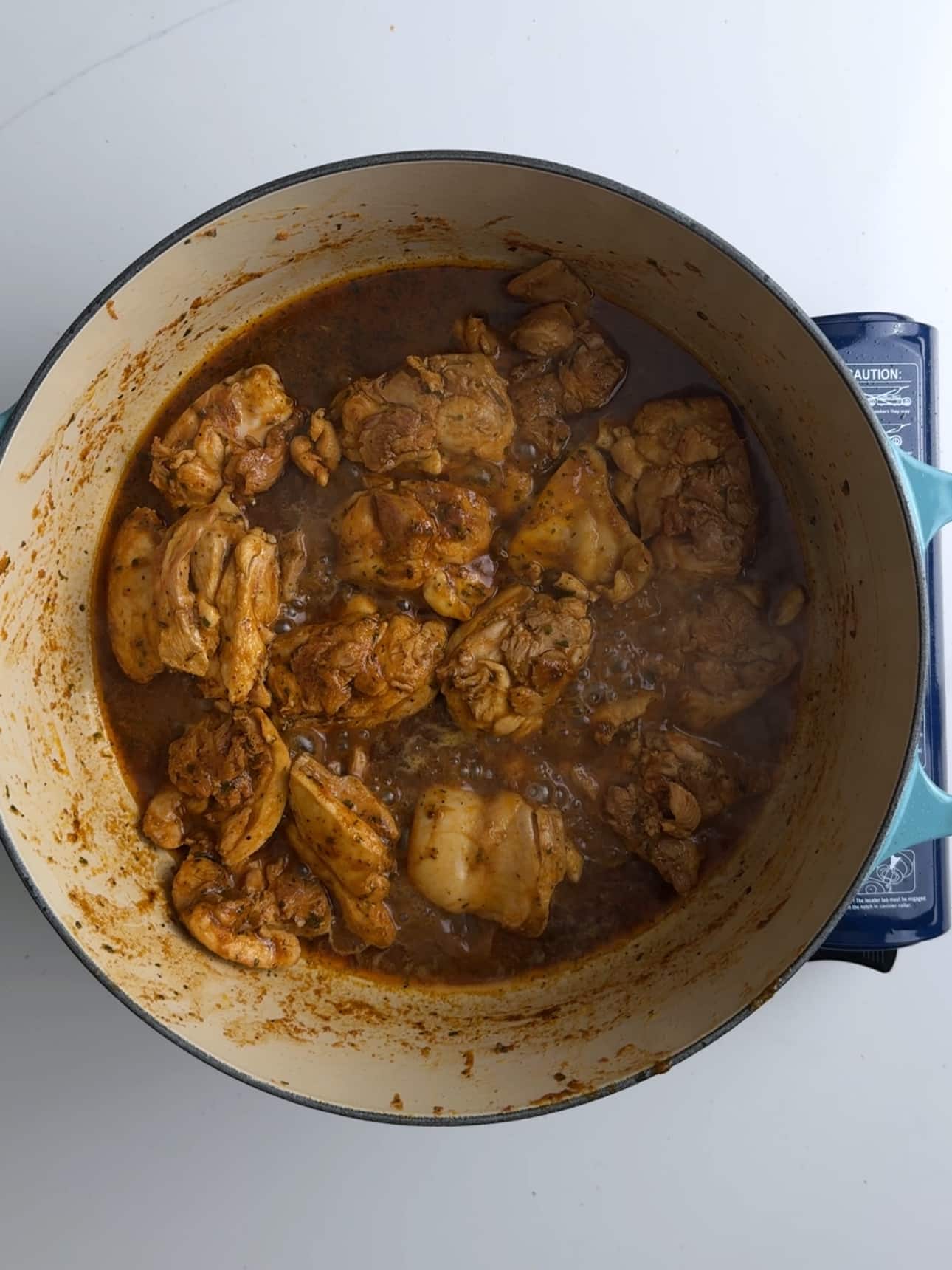 Caribbean Chicken stew in a deep pot. Bubbles are forming on the right side of the pot indicating that the dish is coming up to a boi.