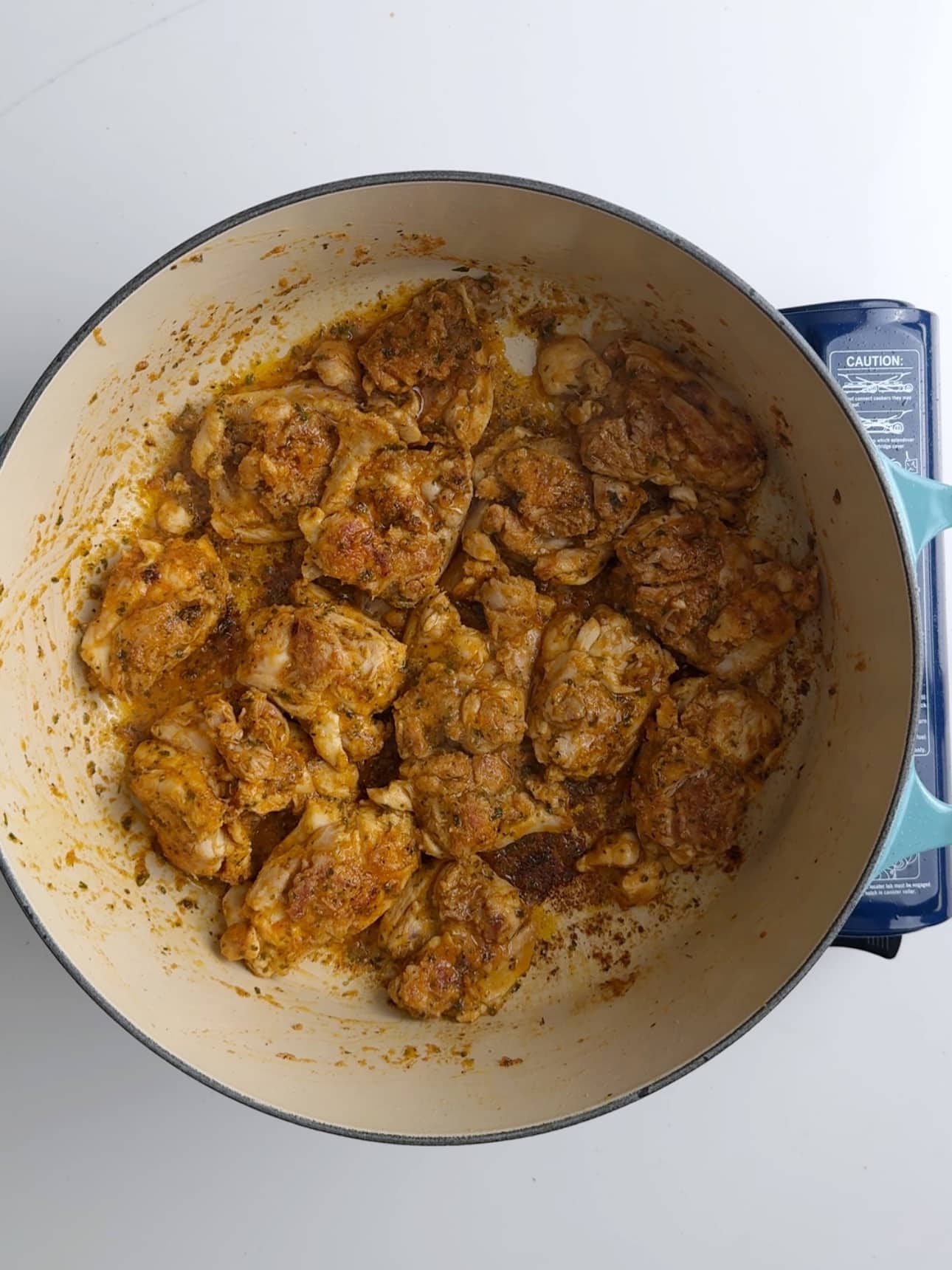 Searing chicken thighs for Caribbean Stew Chicken. Thigh are in a large cast iron skillet with a cream colored base.
