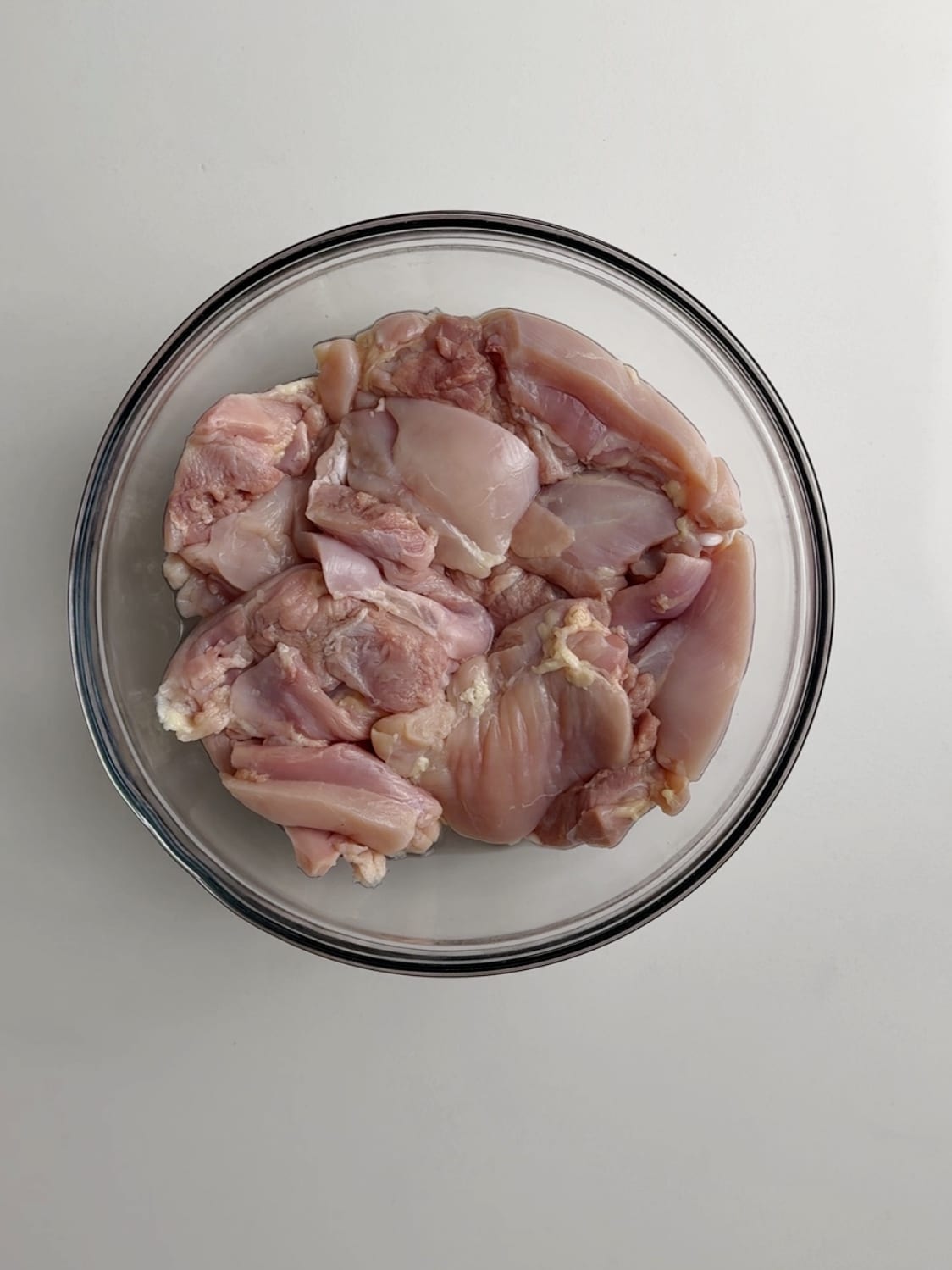 Boneless skinless chicken thighs prepped and in a glass bowl