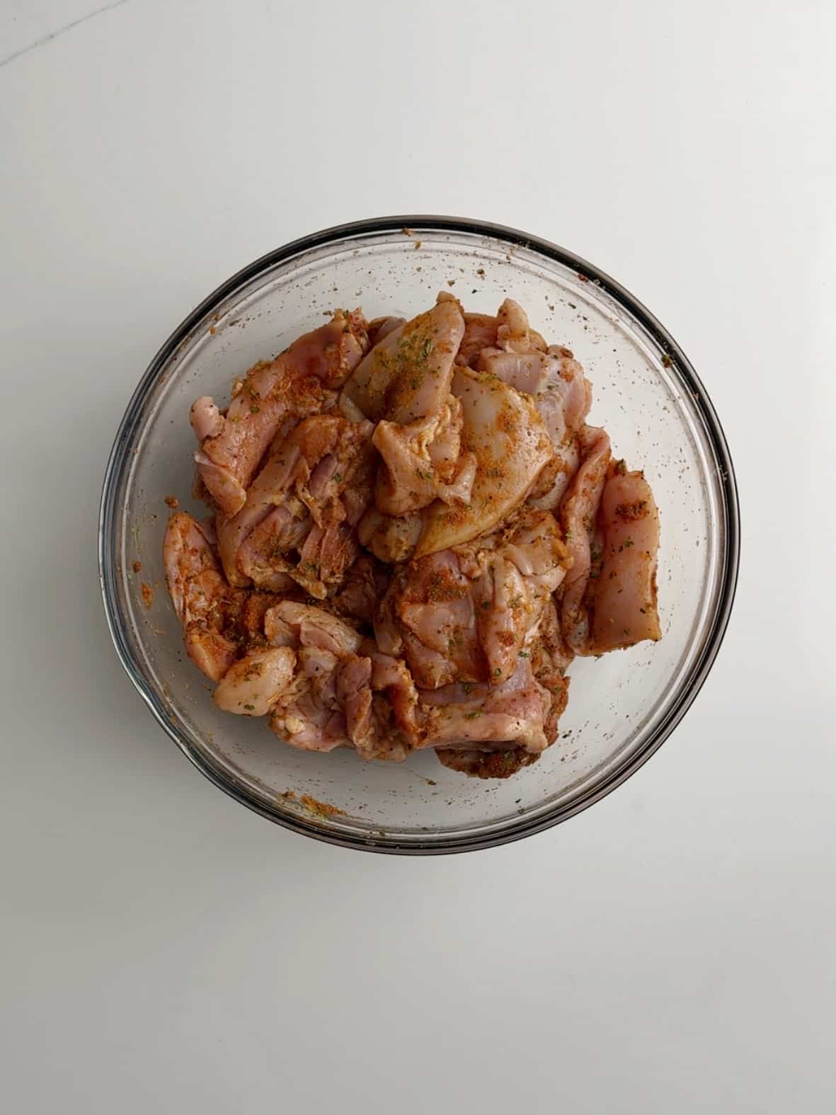 Seasoned chicken thighs in a glass bowl on a white counter for Caribbean Chicken stew.