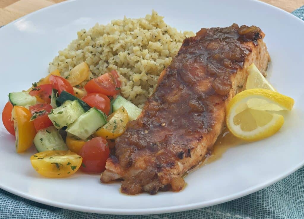 plated grilled salmon topped with sauce and served with veggies and couscous