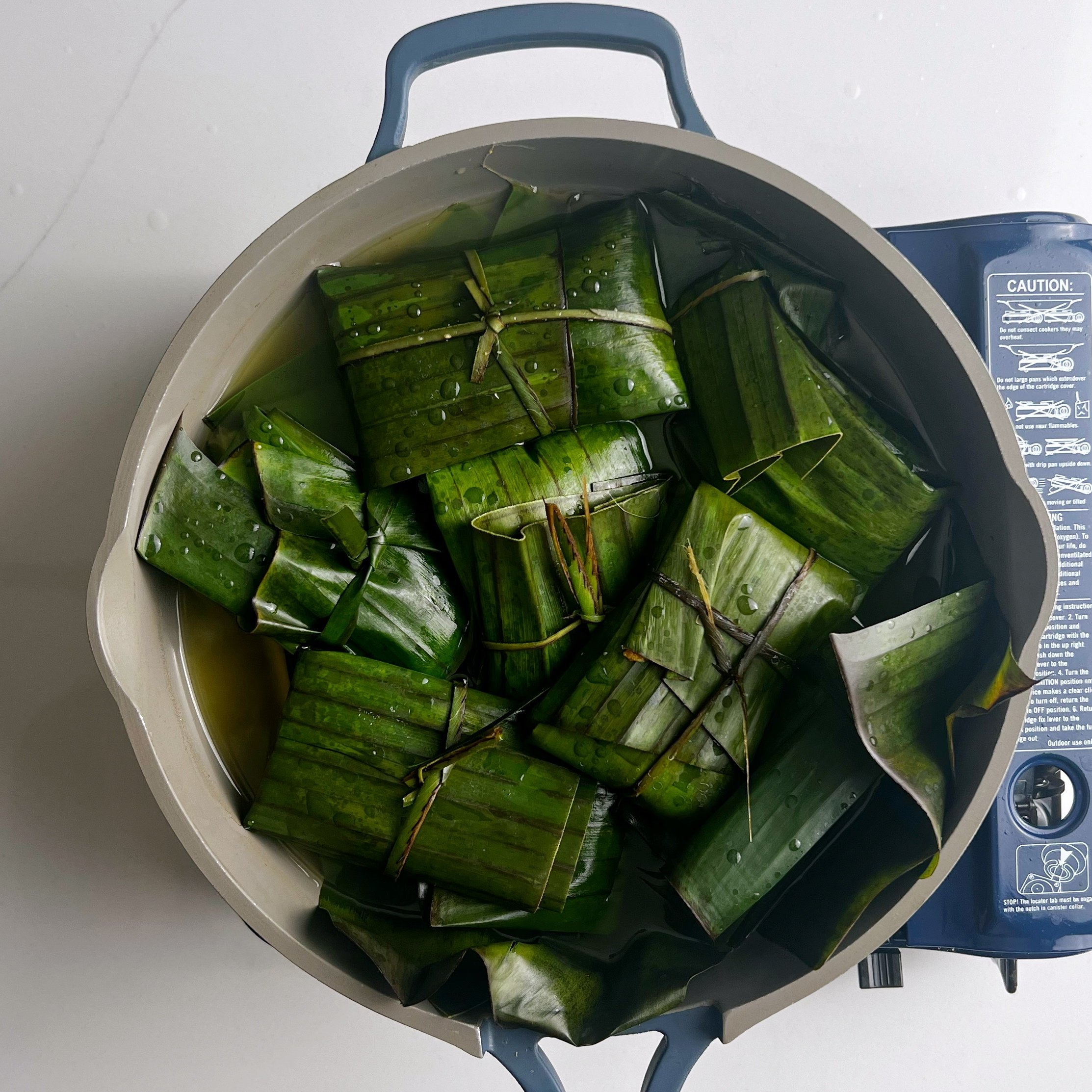 wrapped conkies on banana leaves in a pot of saucpan water