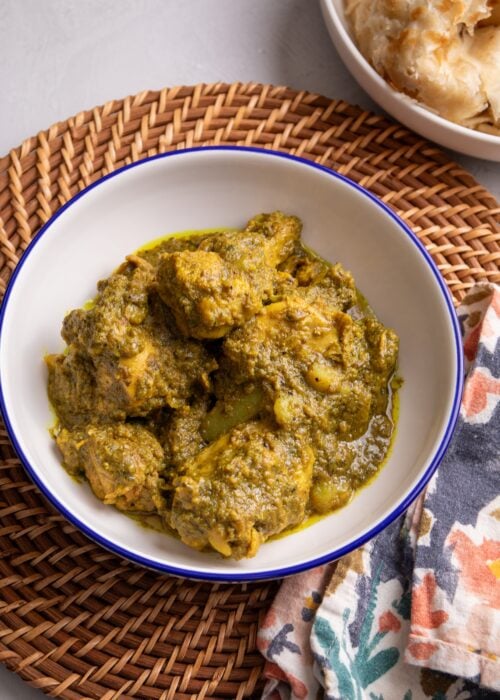 Caribbean Chicken Curry in a Bowl with a bowl with roti visible in the top right hand corner of the image.