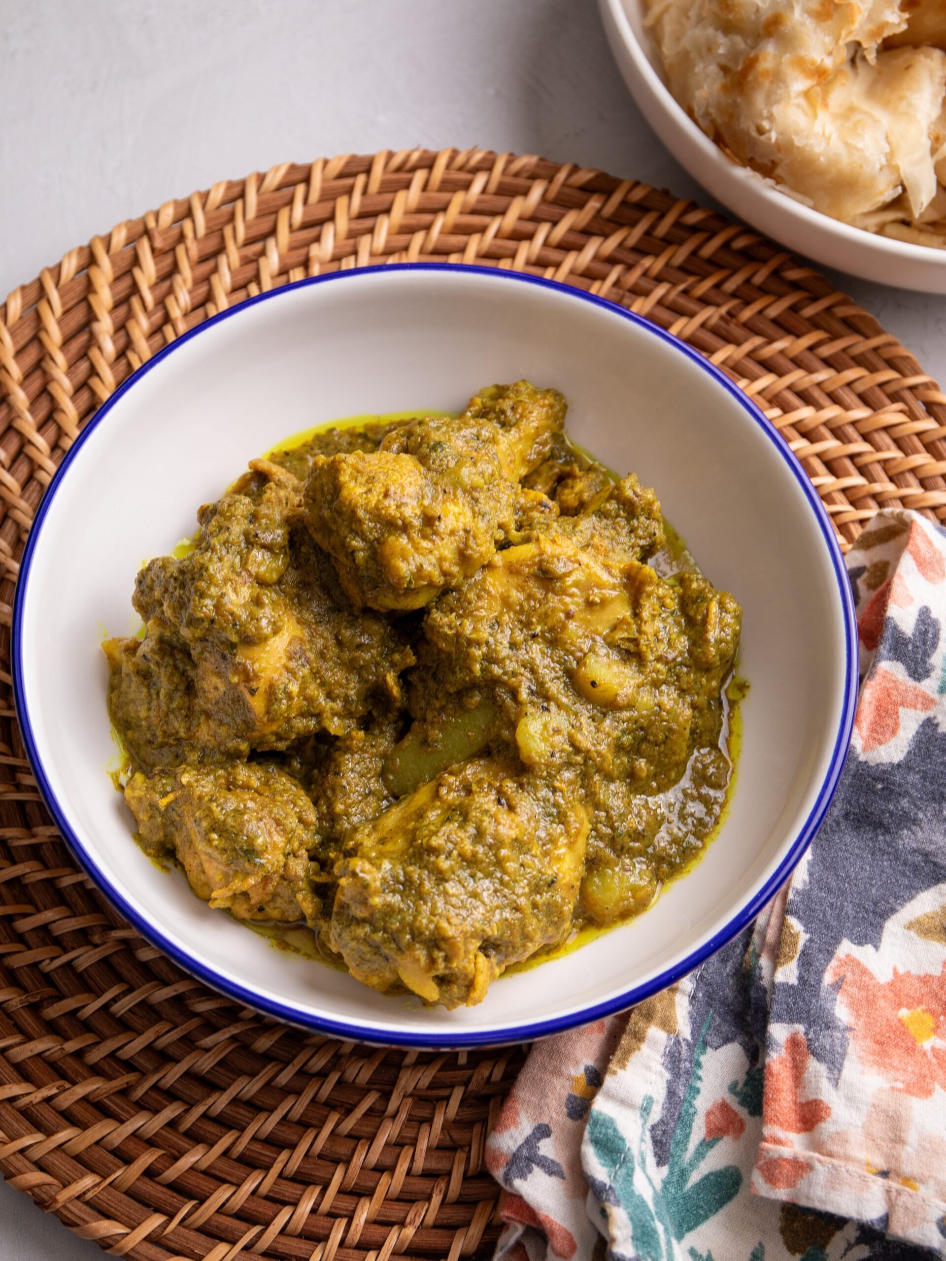 Caribbean Chicken Curry in a Bowl with a bowl with roti visible in the top right hand corner of the image.