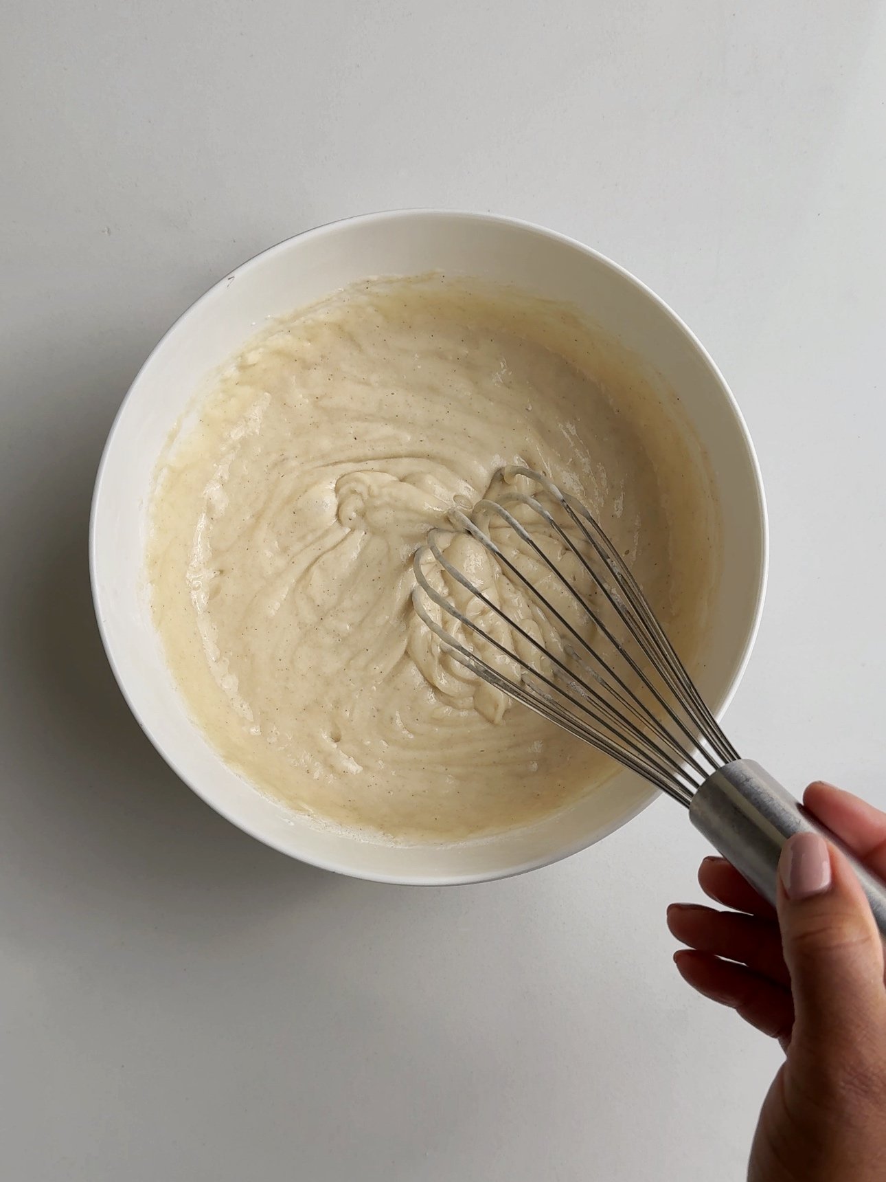 Batter in a bowl with a hand holding a whisk