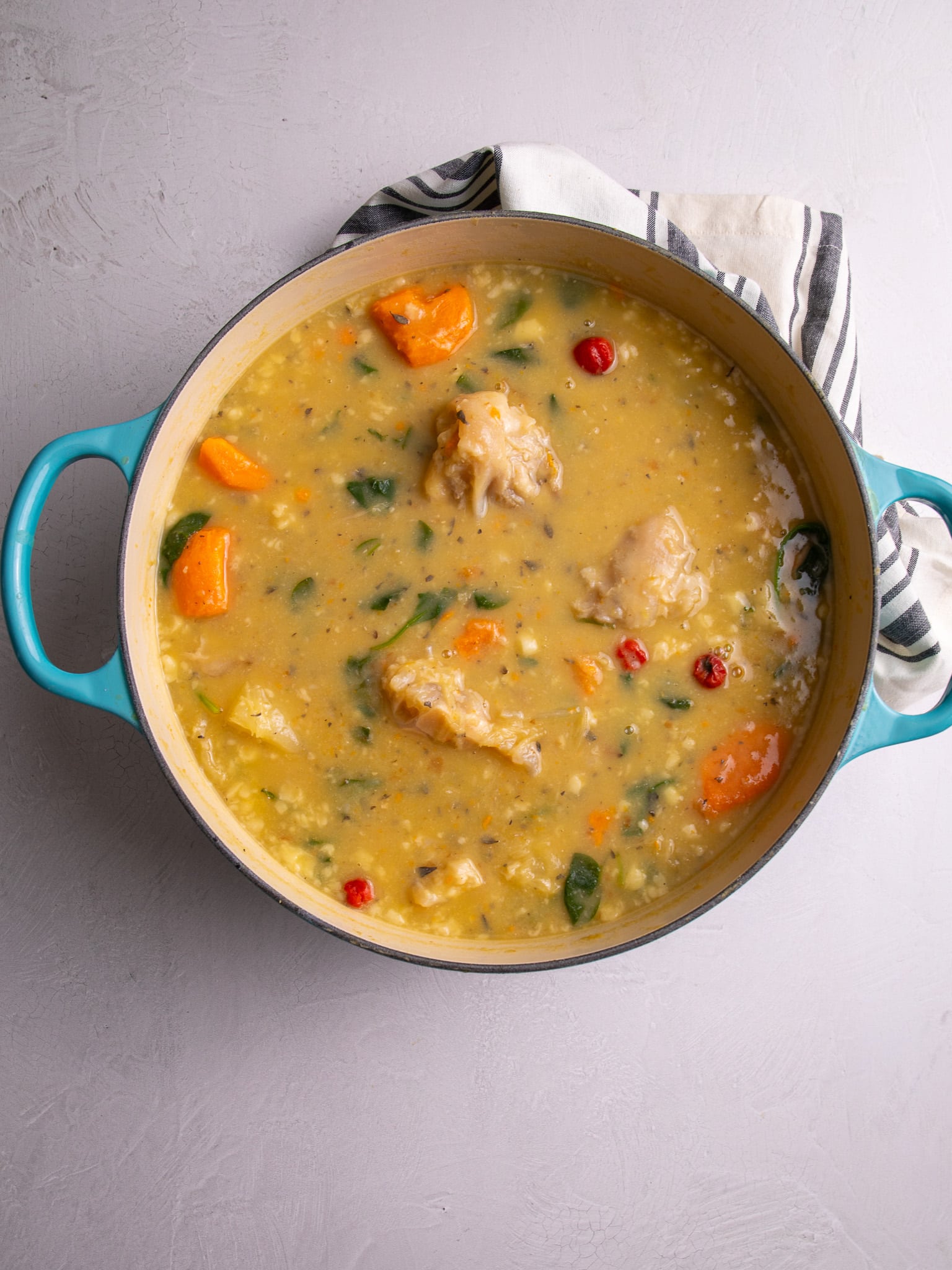 Cow heel soup in a pot with a stripped towel on the side.