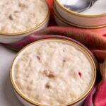 Guyanese sweet rice plated in small bowl. A stack of empty bowls are to the right of the image. All the bowls are on a vibrant shawl with red and orange tones.