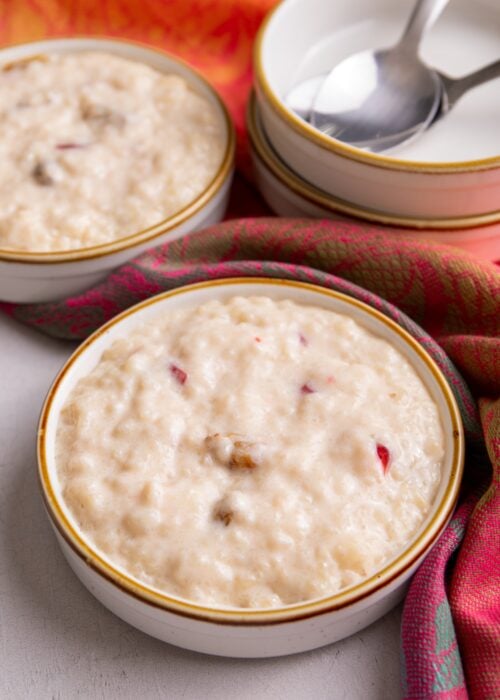 Guyanese sweet rice plated in small bowl. A stack of empty bowls are to the right of the image. All the bowls are on a vibrant shawl with red and orange tones.