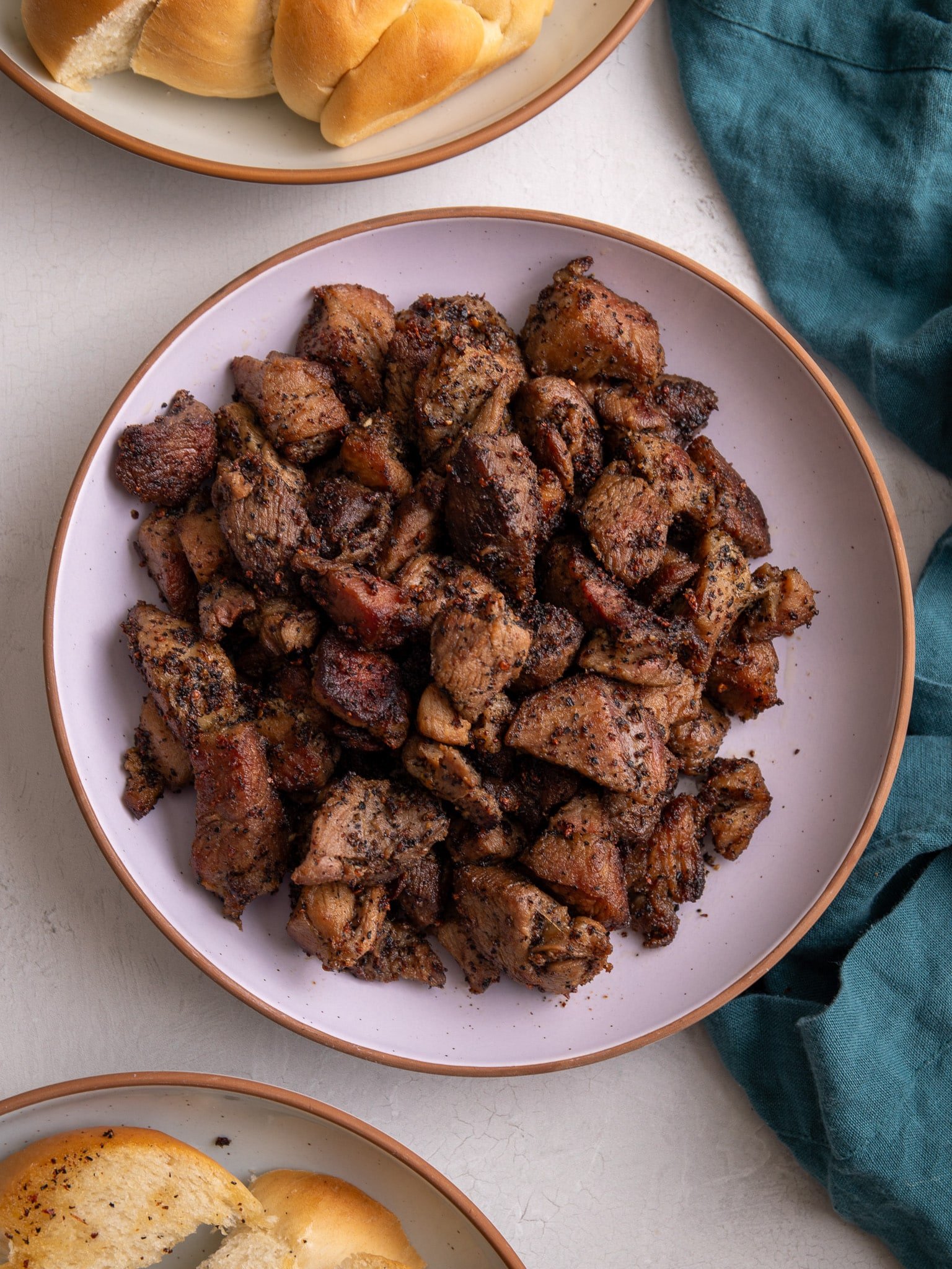 Garlic pork in a pink bowl with plait bread above and below and a teal napkin to the right. 