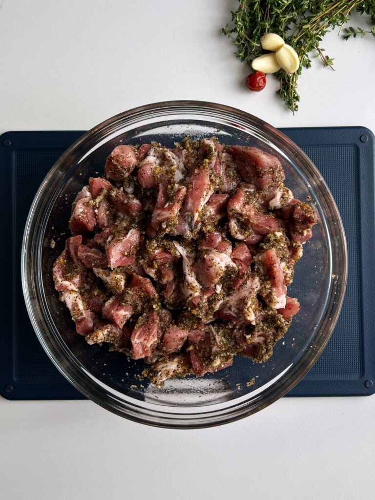 seasoned pork cubes in a class bowl on a gray cutting board