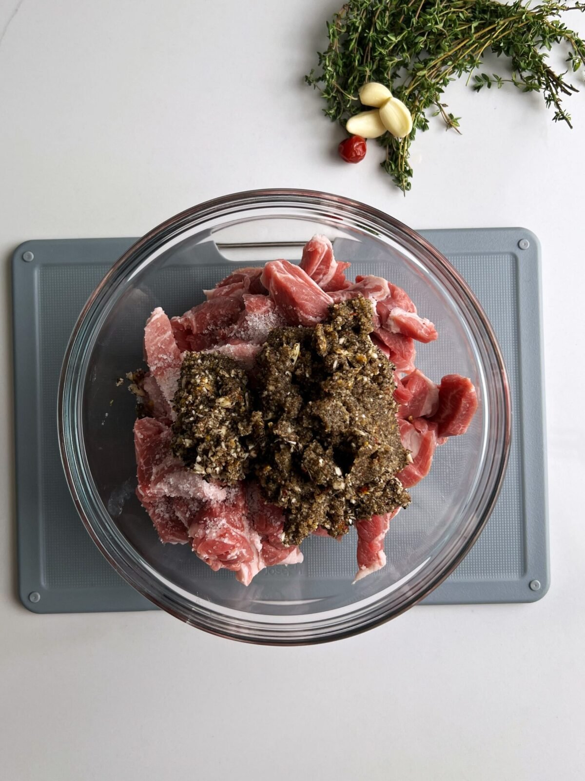 cubed pork with lots of seasoning in a glass bowl, on top of a gray cutting board. First step for garlic pork