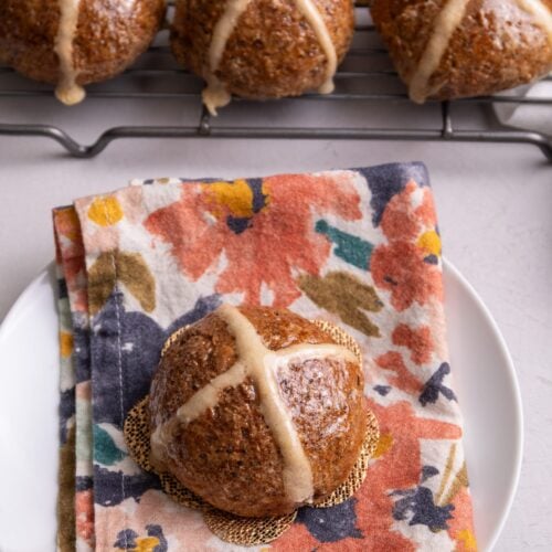 Hot cross buns on a floral napkin on a plate.
