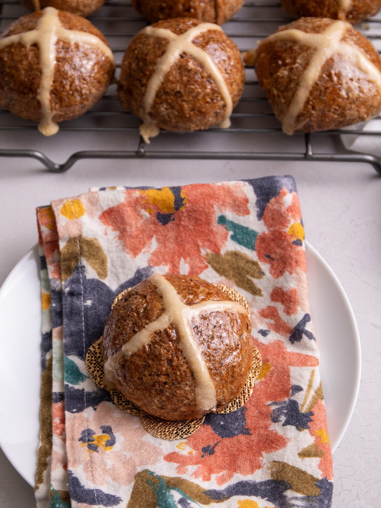 Hot cross buns on a floral napkin on a plate.