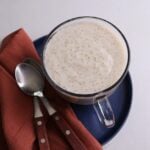 Porridge in a glass cup on blue plate with a rust colored napkin and two spoons with wooden handles.