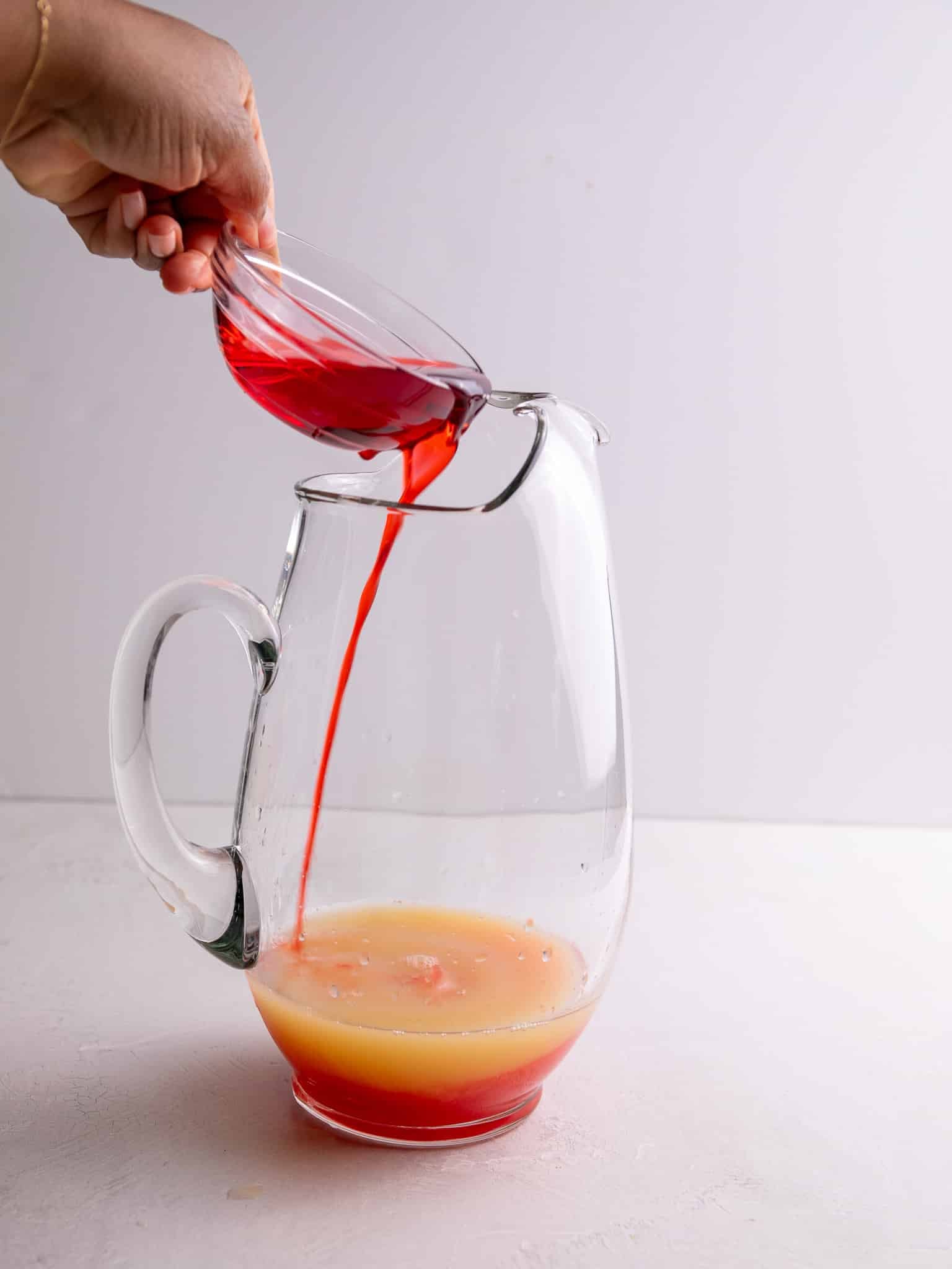 Pouring grenadine into a pitcher for homemade Caribbean rum punch