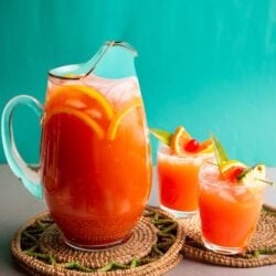 Caribbean rum punch served in a large glass pitcher with tropical garnishes and two glasses over ice