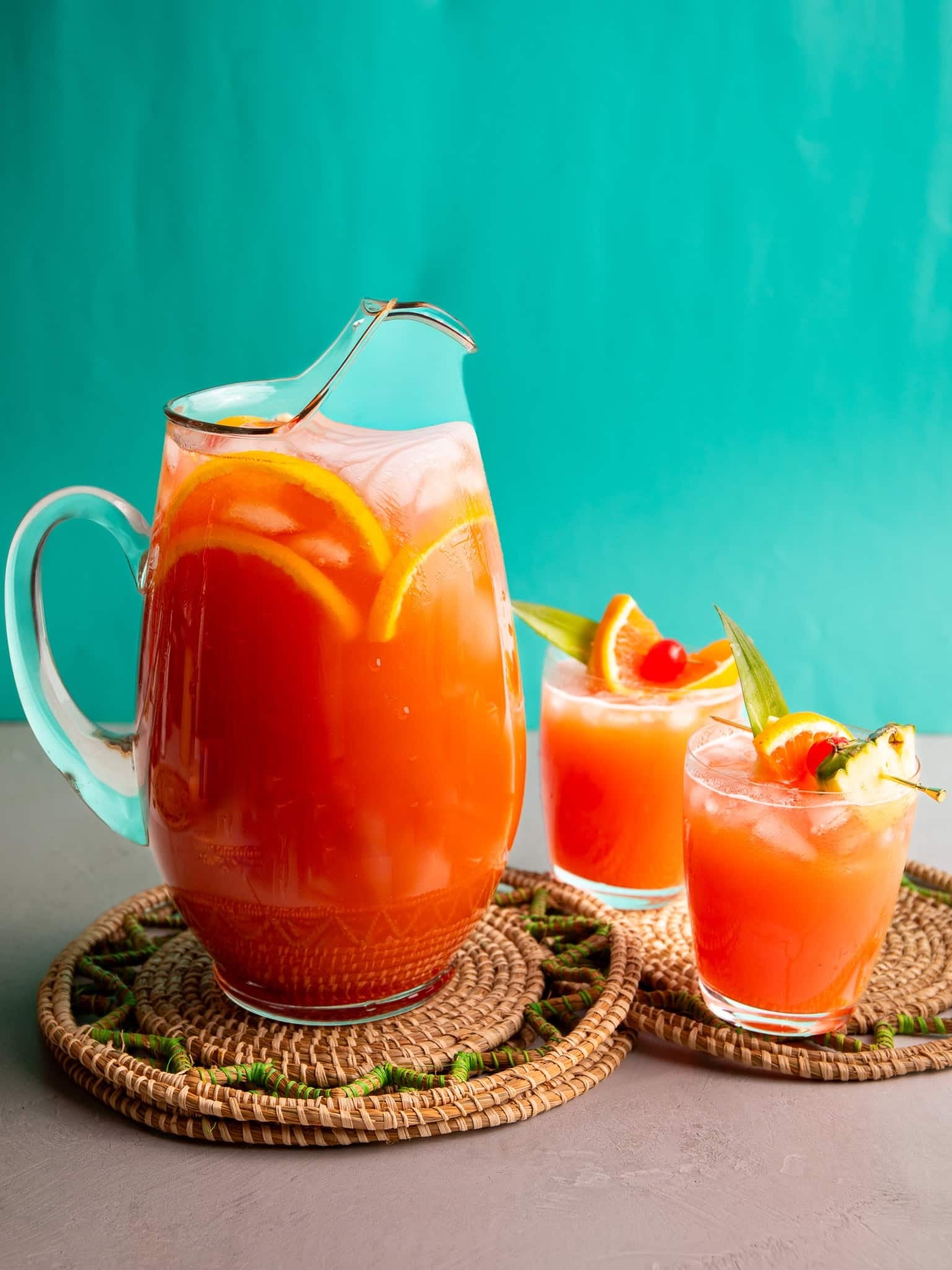 Caribbean rum punch served in a large glass pitcher with tropical garnishes and two glasses over ice