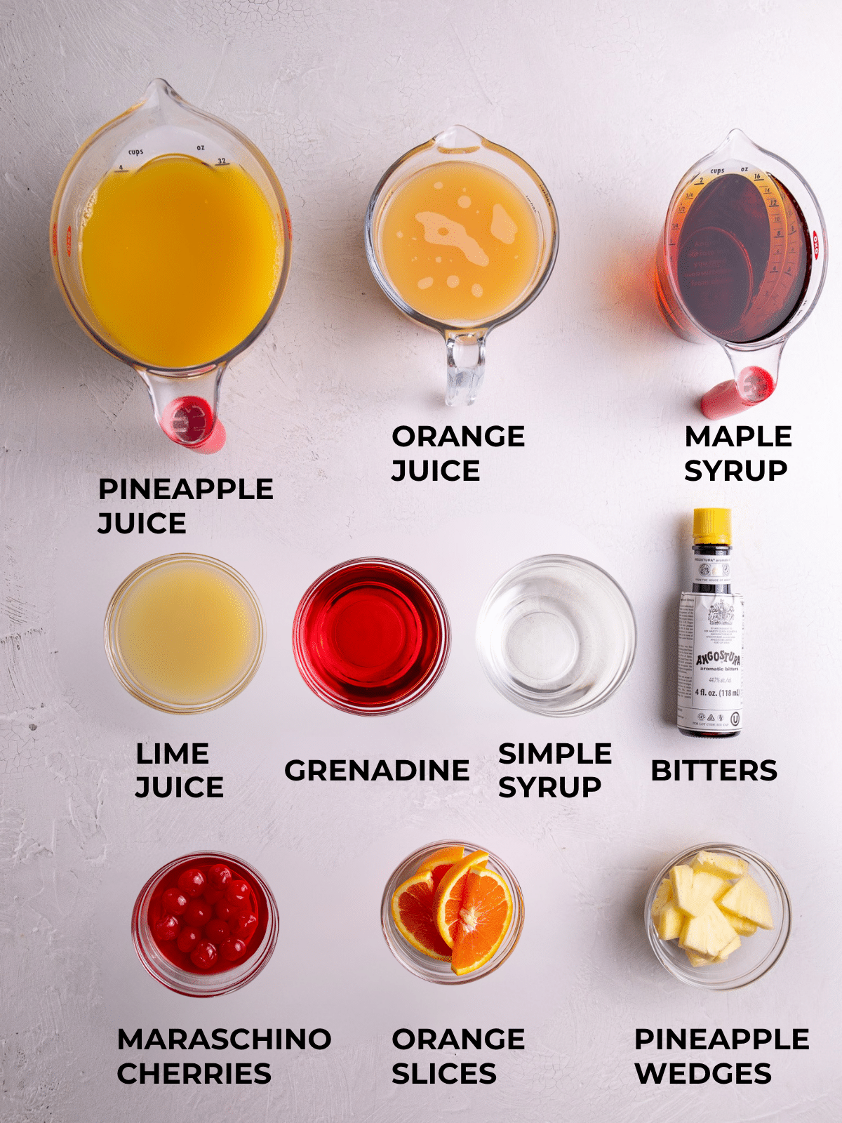 Caribbean rum punch ingredients including pineapple juice, orange juice, lime juice, grenadine, simple syrup, Angostura bitters, maraschino cherries, orange slices, and pineapple wedges laid out on a light background.