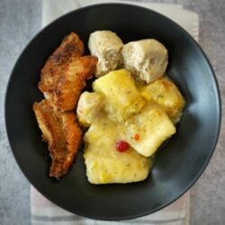 Metemgee, fried fish and gluten free duff in a black bowl on a white and pink napkin on a concrete background