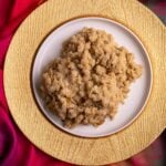 Gluten free parsad on a white plate. The white plate is on a gold charger and the background is a colorful Indian scarf.