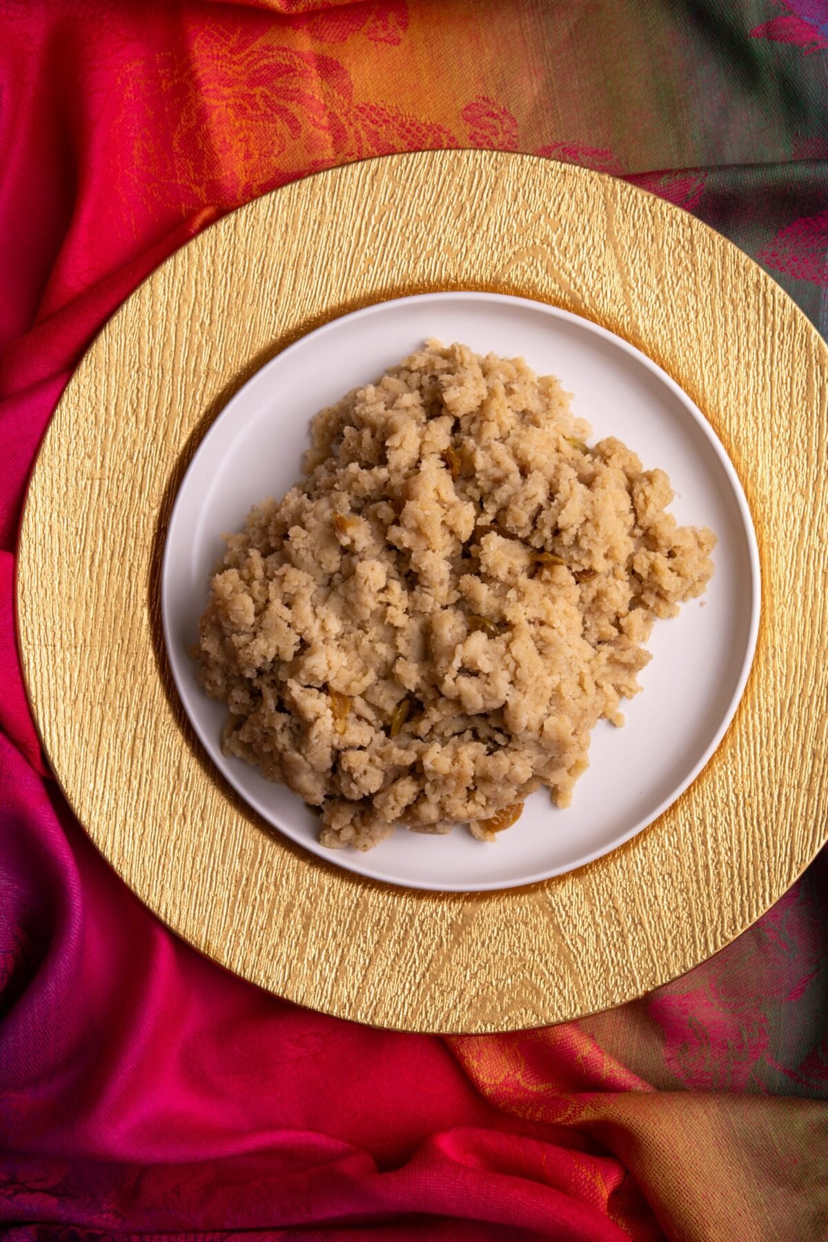 Gluten free parsad on a white plate. The white plate is on a gold charger and the background is a colorful Indian scarf.