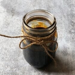 A small mason jar filled with burnt sugar (browning)with a brown twine around the mouth of the jar.