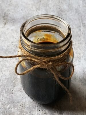 A small mason jar filled with burnt sugar (browning)with a brown twine around the mouth of the jar.